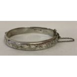 A vintage silver hinged bangle to half floral engraving decoration. Complete with safety chain.