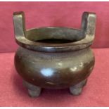 A Chinese bronze censer with loop handles, bulbous bowl and tripod feet.