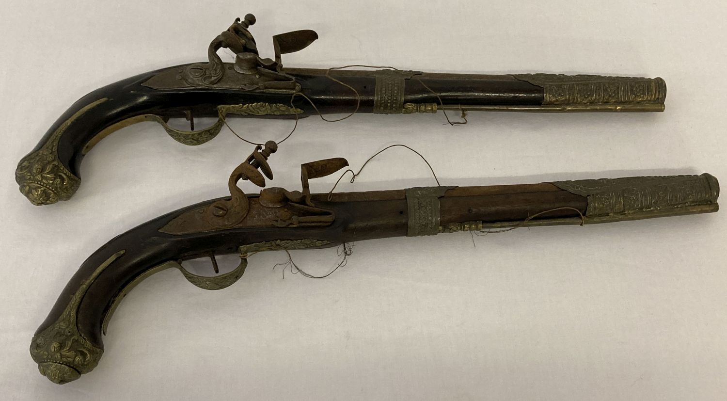 A pair of antique Middle Eastern brass framed flintlock pistols with ornate foliate designs.