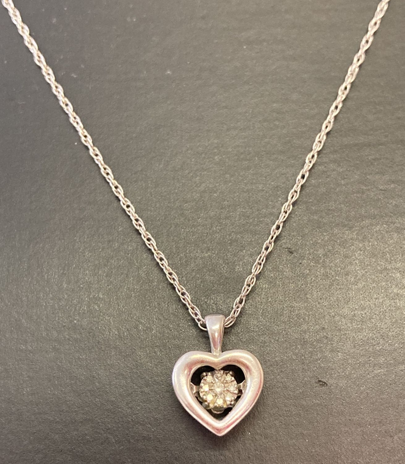 A silver fine rope chain with pierced work heart pendant set with 9 small diamonds.