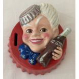 A painted cast iron Coca Cola money bank in the form of a bottle cap with the Coca Cola sprite.