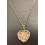 A silver openwork heart shaped locket set with a pale pink oval cut stone and marcasites.