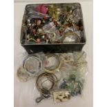 A tin of vintage and modern costume jewellery to include necklaces, bangles & a nurses style watch.