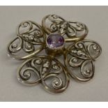 A decorative flower design brooch with scroll design open work and a central round cut amethyst.