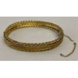 A gold bangle with diamond shaped decoration to centre and twisted rope details to both edges.