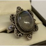 A silver dress ring set with an oval labradorite cabochon stone. Decorative scroll work to mount.