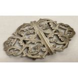 A decorative antique silver buckle with scroll detail and engraved decoration.
