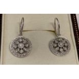 A pair of 9ct white gold and diamond drop earrings in a modern circular and flower design.