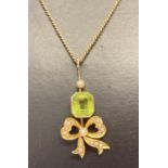 An antique 18ct gold peridot and seed pearl pendant with bow detail on a 14ct gold fine curb chain.