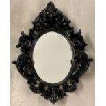 A modern black ornate framed, oval shaped, wall hanging mirror in a gothic style.