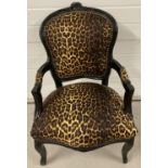 A leopard print upholstered black painted armchair with carved detail to top, arms and legs.