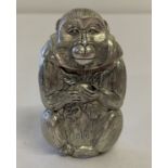 A white metal vesta case in the form of a monkey holding a peach.