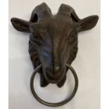 A large cast metal door knocker in the form of a goats head, with ring.