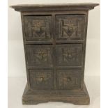 A small dark wood chest of drawers with carved figure decoration throughout.