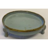 A Chinese porcelain blue glazed dish with copper rim raised on tripod feet.