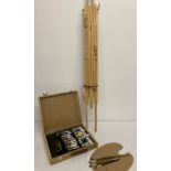 A wooden cased artists box of paints, brushes and pallet together with a large wooden tripod easel.