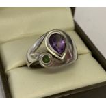 A modern design silver dress ring set with a teardrop cut amethyst and a small round peridot.