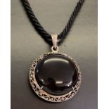 A circular silver & onyx pendant with pierced work decoration, on a cord thong with silver fixings.