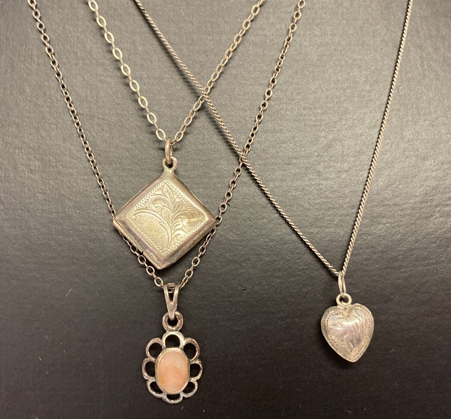 3 silver necklaces. A diamond shaped locket with floral engraving on a fine belcher chain.