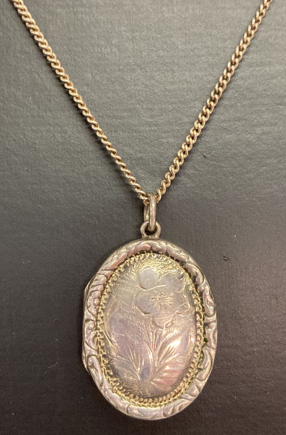 A vintage silver oval shaped locket with floral decoration to front, on a 22" curb chain.