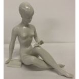 A Royal Dux figurine of a naked woman sitting with a book and a butterfly on her knee.