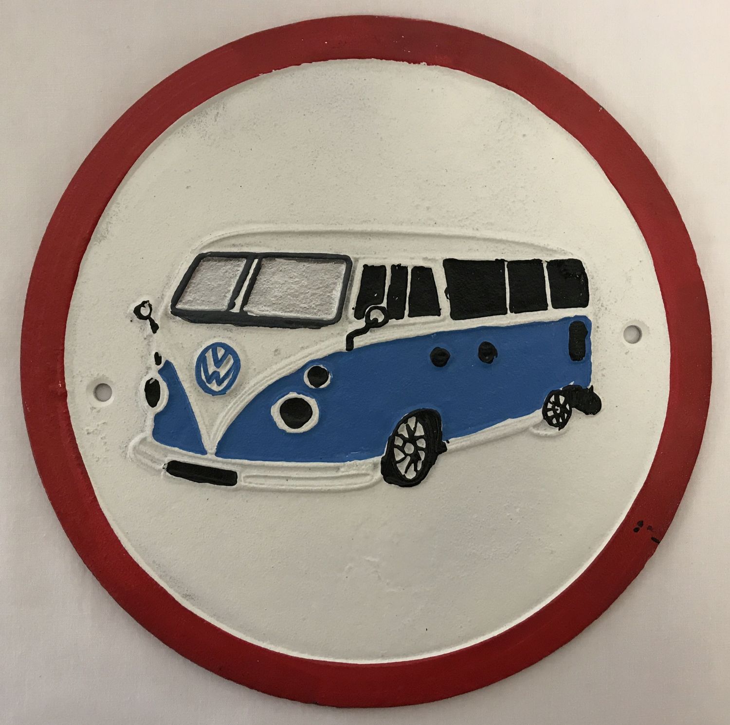 A circular shaped painted cast iron wall plaque depicting a VW camper van.