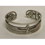 A decorative white metal open work bangle with Egyptian goddess Isis and scarab beetle detail.