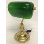 A modern brass desk lamp with green glass tilting shade.