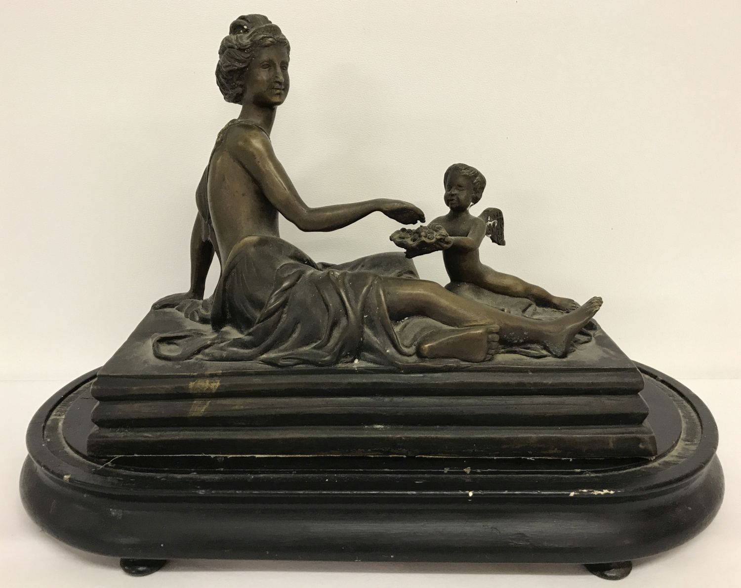 A filled bronze figure of a reclining semi naked classical female with cherub offering fruit.