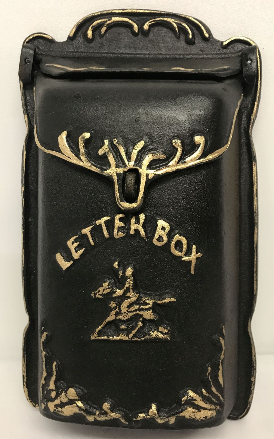 A cast metal wall hanging letter box, painted black with gold detailing and hinged opening lid.