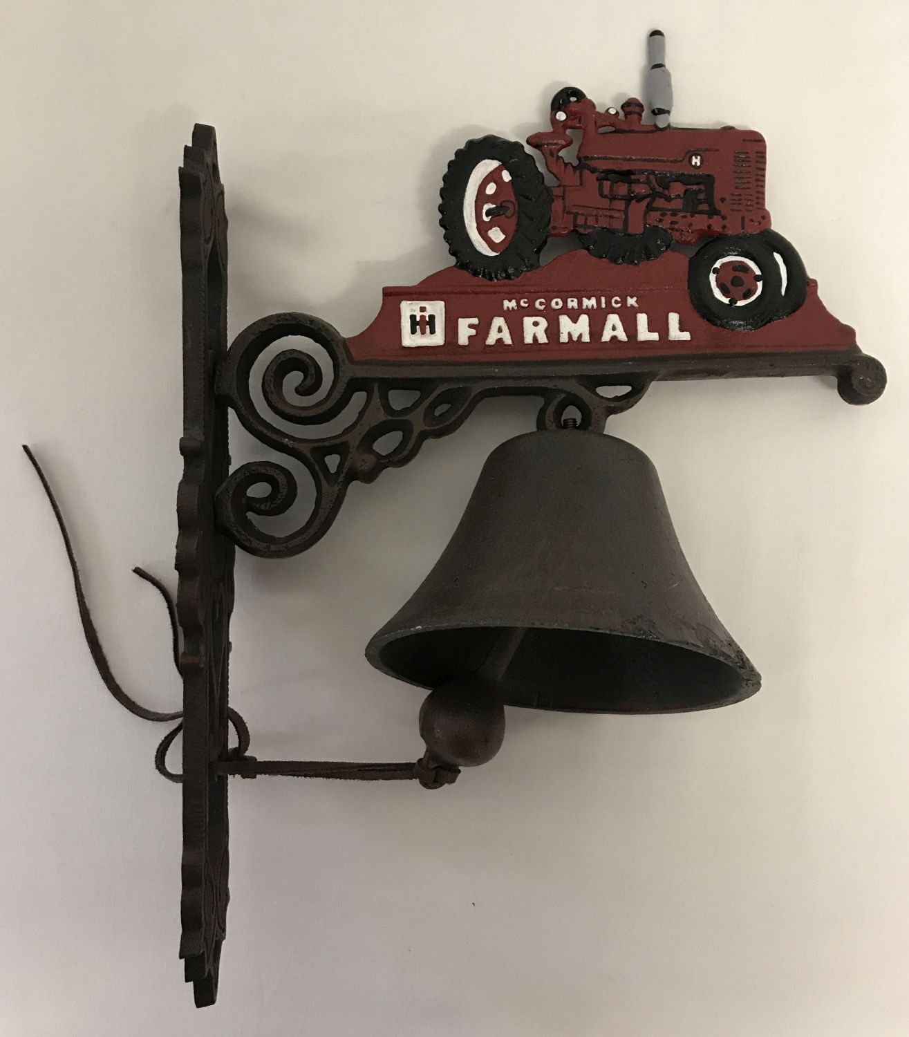 A cast metal wall hanging garden bell with McCormick Farmall tractor decoration.