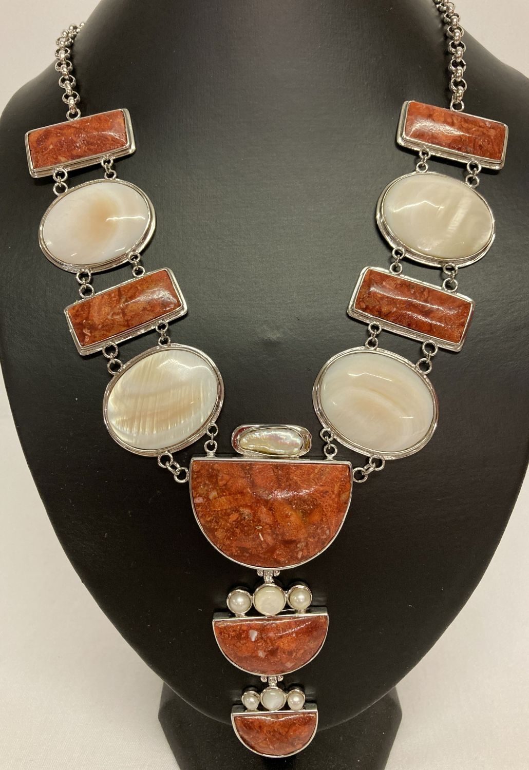 A large white metal statement necklace set with mother of pearl, keshi pearl and red stones.