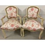 A pair of Louis XV style wooden framed armchairs, painted cream, with floral upholstery.