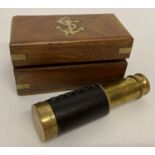 A reproduction small brass telescope in a wooden box with brass inlay detail.