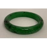 A Chinese green jade bangle with carved floral detail.
