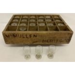 A vintage wooden glass crate stamped McMullen Hereford containing 22 small liqueur glasses.