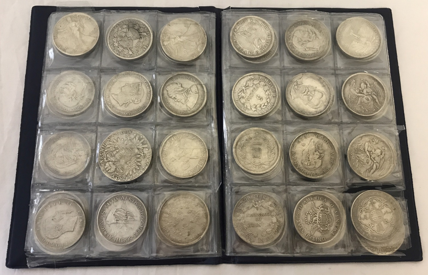 A folder containing 70 assorted white metal coins from around the world.