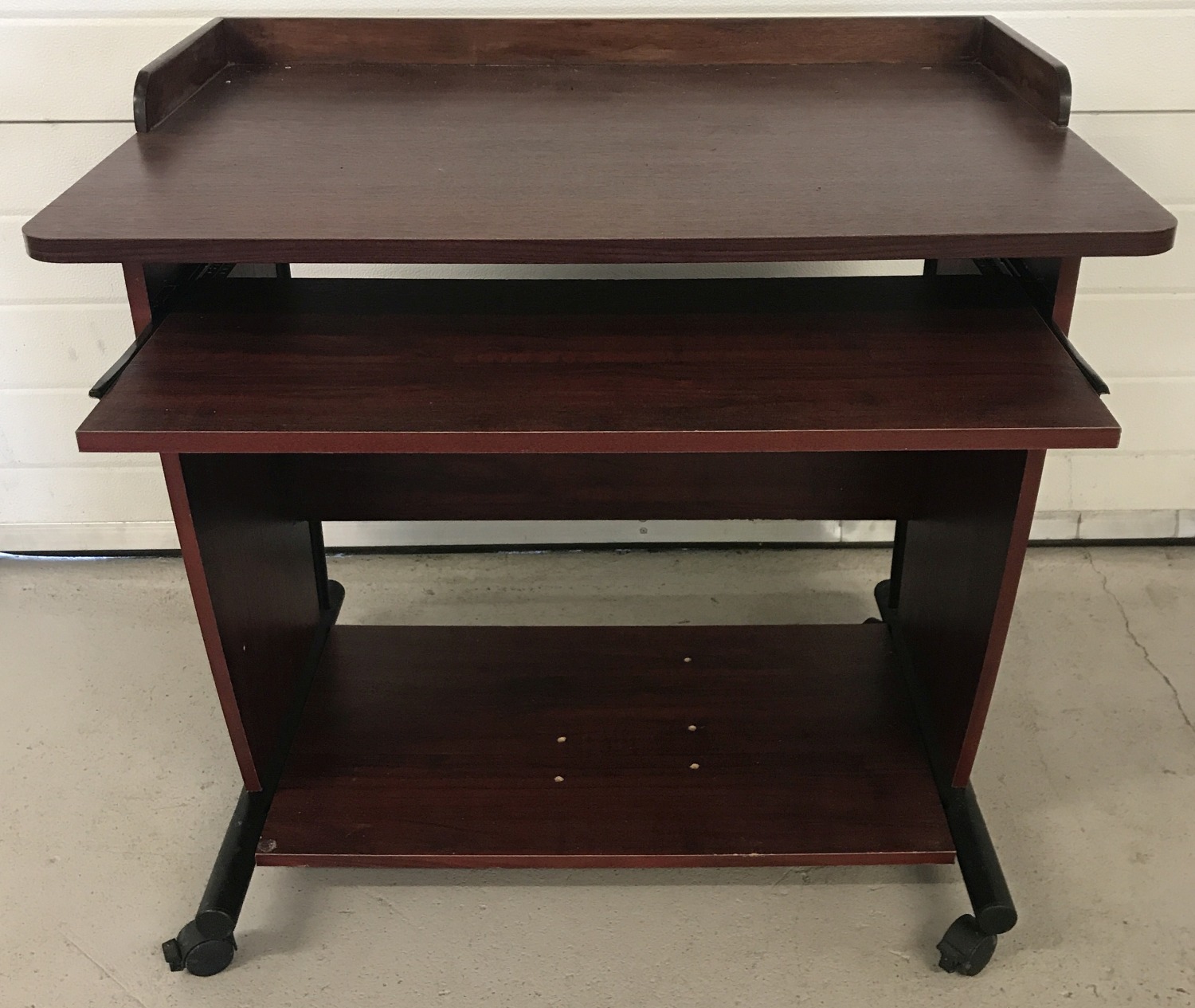 A modern dark wood effect computer table on wheels.