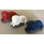 3 stone garden ornaments in the shape of laying lions, painted in red, white and blue colours.