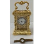 A heavily gilded ornamental miniature carriage clock with enamelled face.