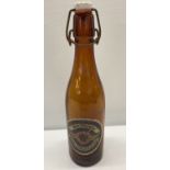 A WWII style brown glass beer bottle with German paper label and ceramic stopper.