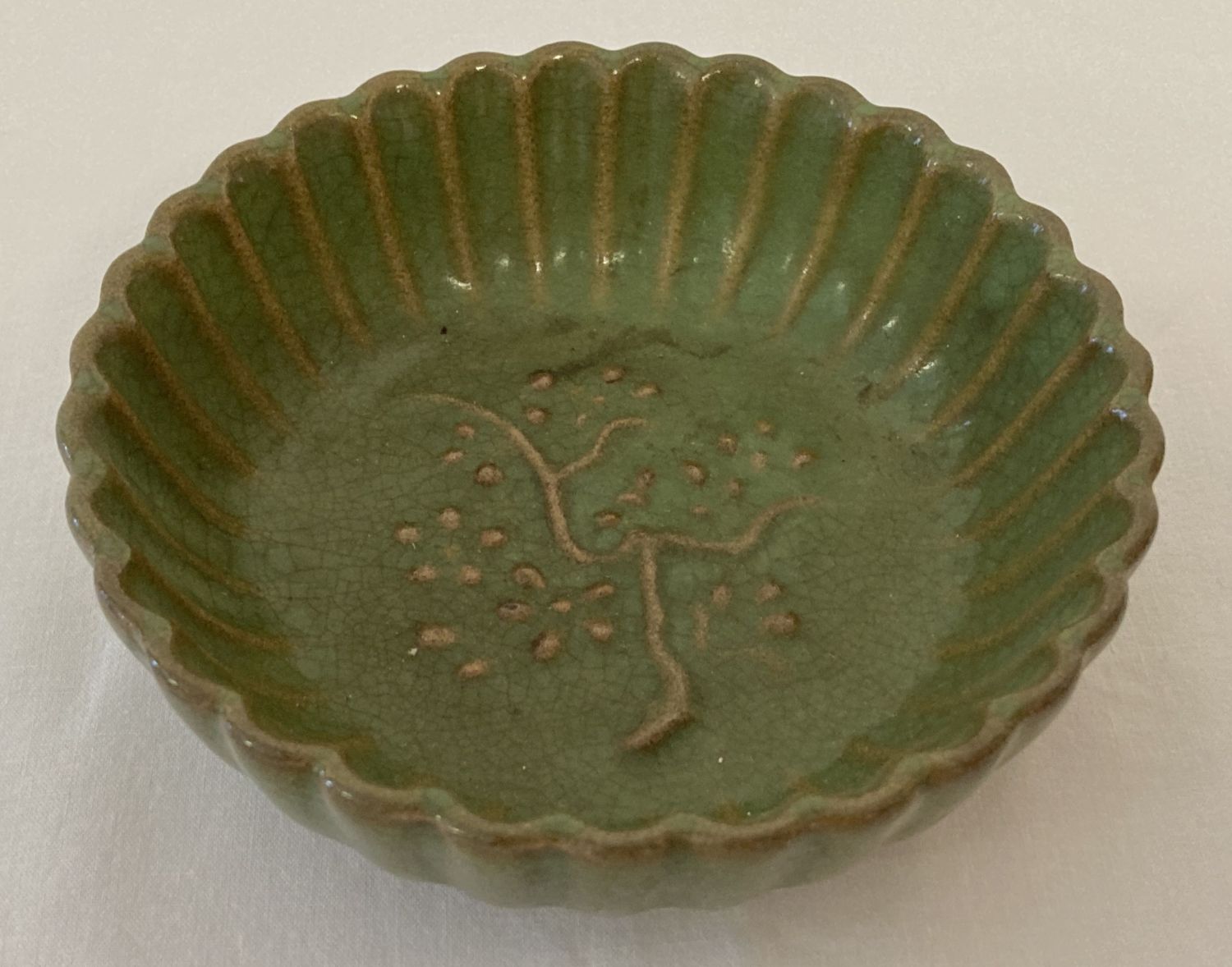 A small dark green glazed bowl with scalloped sides and tree detail to interior.