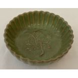A small dark green glazed bowl with scalloped sides and tree detail to interior.