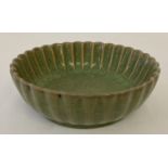 A small round ceramic dish with scalloped rim and dark green crackle glaze.