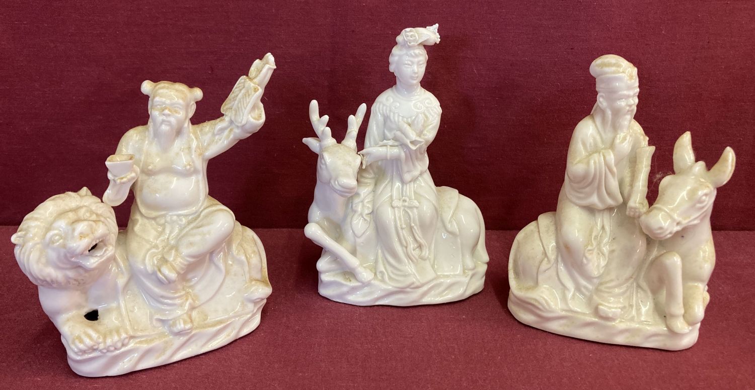 3 Chinese ceramic blanc de chine figurines depicting figures sitting atop animals.