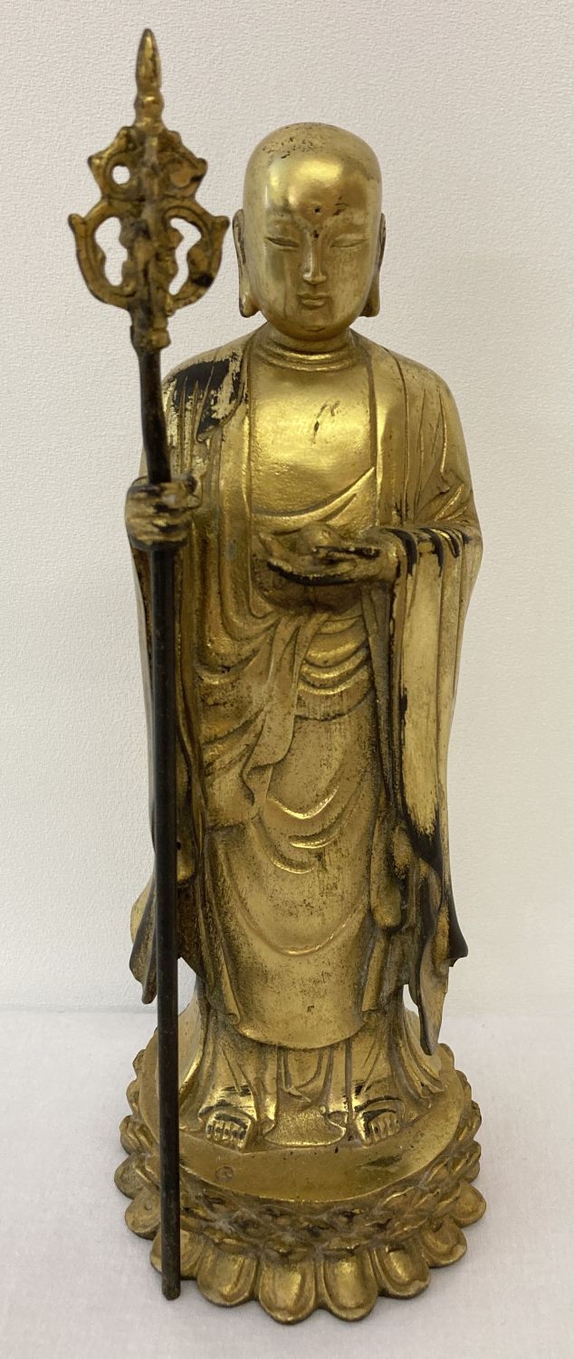 A gilt hollow bronze figure of an Oriental Deity holding a staff stood atop a lotus flower.