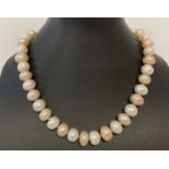 A 16" string of larger oval shaped alternate cream & peach freshwater pearls, with magnetic clasp.