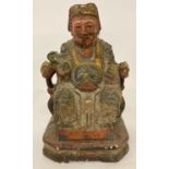 A painted wooden figurine of a seated Oriental Deity holding a sceptre.
