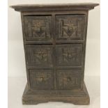 A small dark wood chest of drawers with carved Aztec figure decoration throughout.
