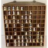 A collection of 57 ceramic and wooden thimbles in a wooden collectors wall hanging display case.